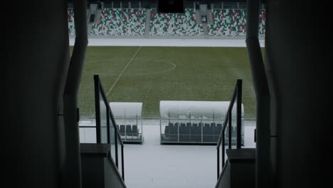 Empty-outdoor-football-soccer-stadium-field-covered-with-snow-in-winter,-light-snowfall.-Shot-with-2x-anamorphic-lens